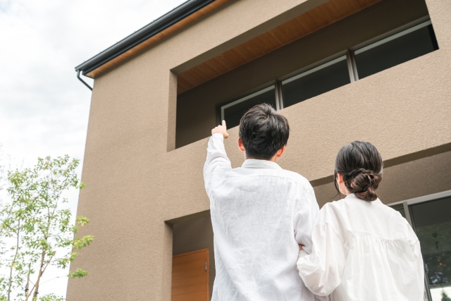 完成した住宅の前で建物を指差す夫婦の後ろ姿