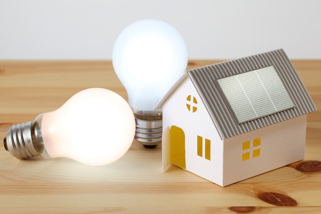 太陽光パネル付きの家の模型と電球が並ぶ省エネ住宅のイメージ